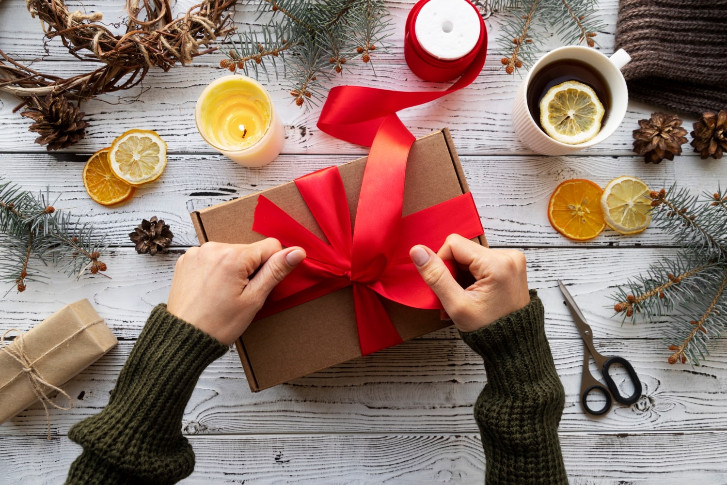 Hands wrapping a personalized gift with festive ribbon and natural decorations